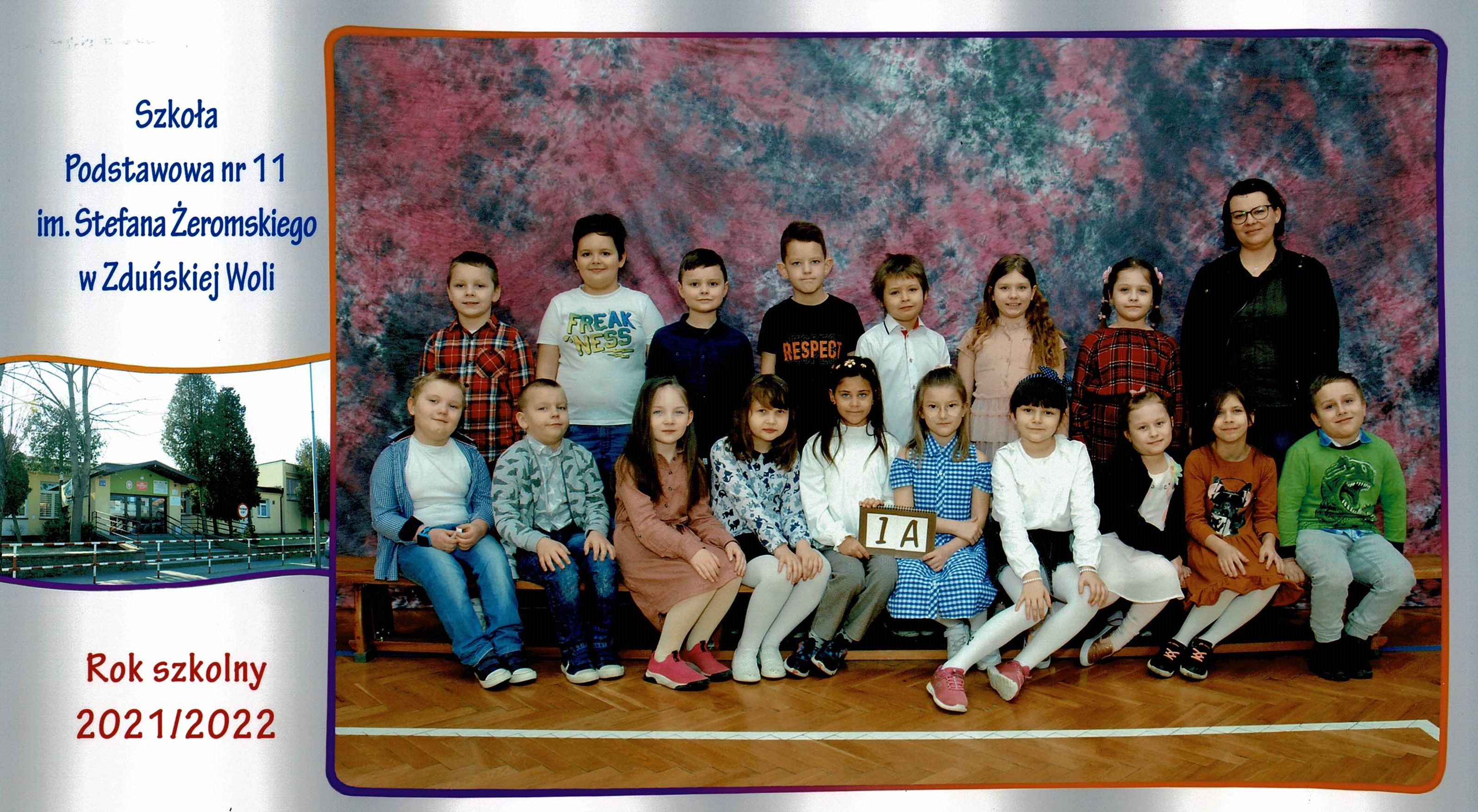 Uczniowie klasy 1A, dziewczynki i chłopcy siedzący na ławce z tabliczką "klasa 1a"